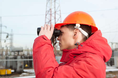 Engineer at Electrical Substation looks through a binoculars. Electrical power industryの写真素材