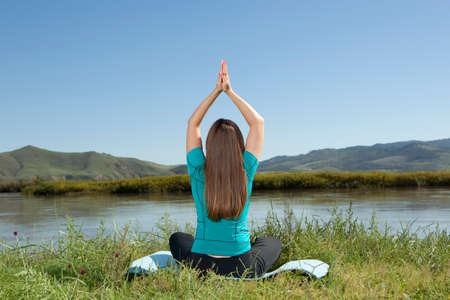 Young woman is practicing yoga at mountain river, relax in natureの写真素材