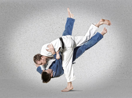 The two judokas fighters fighting men on gray background
