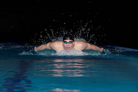 Young man in black cap in swimming pool. Butterfly style
