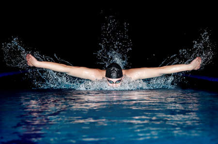 Young man in black cap in swimming pool. Butterfly styleの写真素材