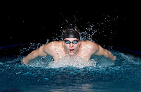 Young man in black cap in swimming pool. Butterfly styleの写真素材