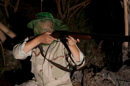 Night poacher. Man in mosquito net ready to hunt with hunting rifle