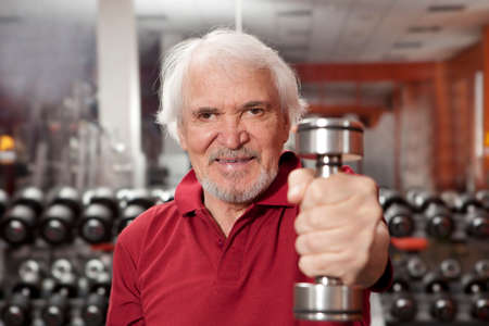 Attractive senior man in gym working out with weightsの写真素材
