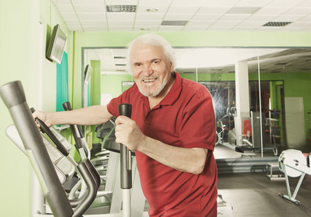 Senior man uses elliptical cross trainer in gymの写真素材