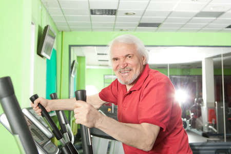 Senior man uses elliptical cross trainer in gymの写真素材
