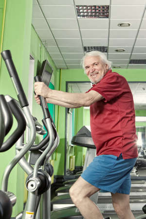 Senior man uses elliptical cross trainer in gymの写真素材