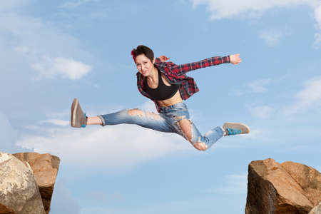 Young woman jumping over the gap at blue skyの写真素材
