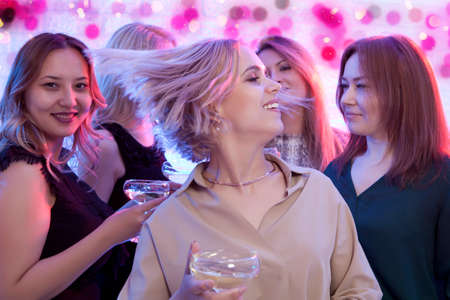 Blonde woman looking at camera while dancing at nightclub among her friendsの写真素材