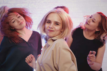 Blonde woman looking at camera while dancing at nightclub among her friendsの写真素材