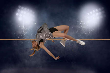 Woman in action of high jump a stadium at nightの写真素材