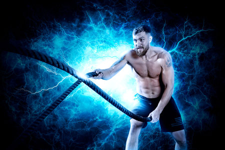 Crossfit training. Man working out with battle ropes at gym