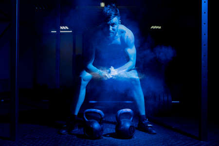 Weightlifter clapping hands and preparing for workout at a gym. Focus on dustの写真素材