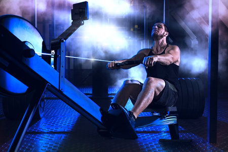 Bearded fit man using rowing machine at functional training gym