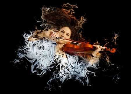 Playing the violin. Young woman playing violin on smoke backgroundの写真素材