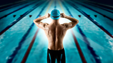 Professional young muscular swimmer jumping from starting block in a swimming poolの写真素材