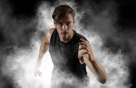 Sporty young man running on black smoke backgroundの写真素材