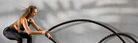 Woman working out with battle ropes. Concept of sport, movement, energy, dynamic, healthy lifestyleの写真素材