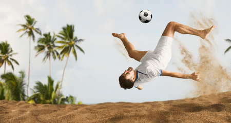The man footballers are desperately playing beach soccer on sand on a sunny day. Man doing kick on...