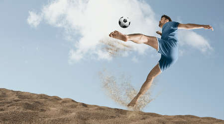 The man footballers are desperately playing beach soccer on sand on a sunny day. Man doing kick on beach with soccer ballの写真素材