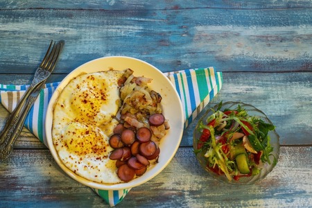 Scrambled eggs with bacon, onion and sausage. On a plate on the table.の写真素材