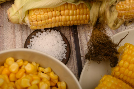 Two boiled ears of corn, corn kernels, coarse salt and raw ears of corn on a wooden table. Fitness...