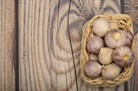A few heads of young garlic in a wicker basket on a wooden background. Autumn harvest. Modern agriculture. Close upの写真素材