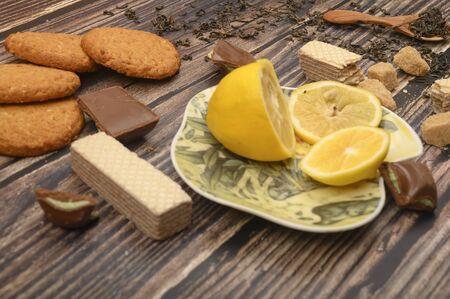 sliced lemon on a saucer, pieces of brown sugar, oatmeal cookies, waffles, pieces of chocolate on a wooden background. Close upの写真素材