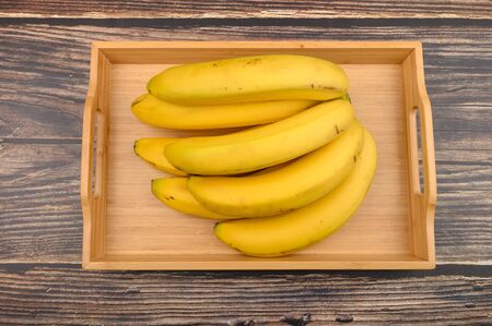 Bunch of ripe yellow bananas on a wooden tray on a wooden background. Close upの写真素材