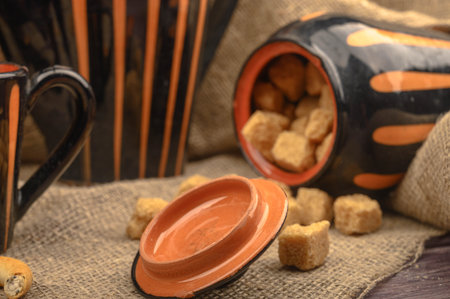 Pieces of brown sugar, a sugar bowl, and pottery against a background of coarse homespun cloth....