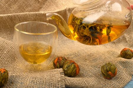 A ball of flower tea brewed in a glass teapot, a glass of tea and several balls of flower tea on a background of rough homespun fabric. Close upの写真素材