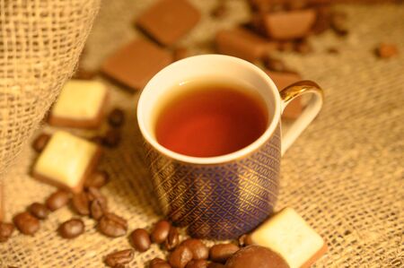 A mug of tea, chocolate and coffee beans on a background of rough homespun fabric. Close upの写真素材