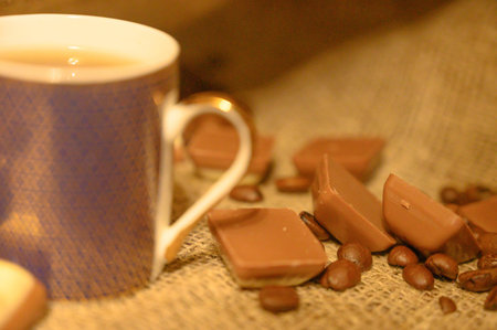 A mug of tea, chocolate and coffee beans on a background of rough homespun fabric. Close up