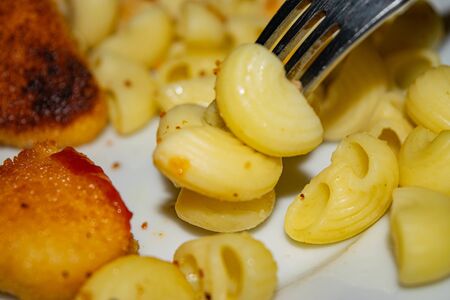 A few boiled macaroni on a fork and a white plate with fried chicken nuggets, macaroni and ketchup on a dark background. Close upの写真素材