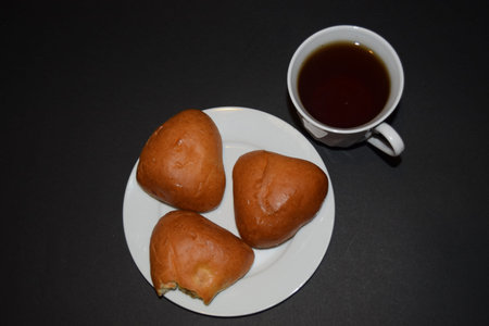 Three pies on a white plate and a Cup of coffee on a black background. Close-up view from above