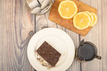Tea in a faceted glass in a vintage Cup holder, tea bags in a glass vase, sliced lemon on a Board and a piece of waffle cake on a white plate on a wooden background. Close upの写真素材
