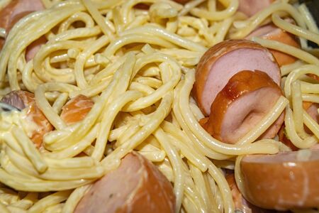 Boiled spaghetti with sauce and boiled sausages cut into pieces on a plate. Close upの写真素材