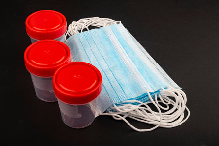 Disposable medical masks and plastic containers for collecting tests on a black background....