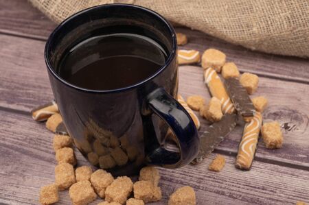 Dark blue ceramic tea mug, cookie sticks with chocolate and white icing , and pieces of brown cane sugar. Close upの写真素材