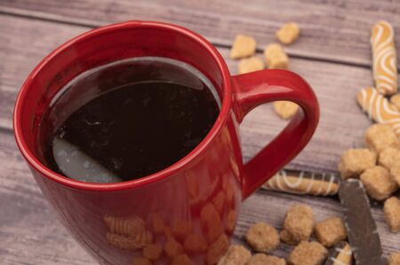 A red ceramic tea mug, cookie sticks with chocolate and white icing, and pieces of brown cane sugar on a wooden background. Close upの写真素材