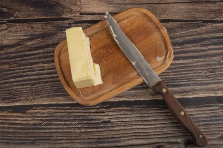A wooden plate with a piece of butter and a knife with a wooden handle on a wooden background. Close upの写真素材