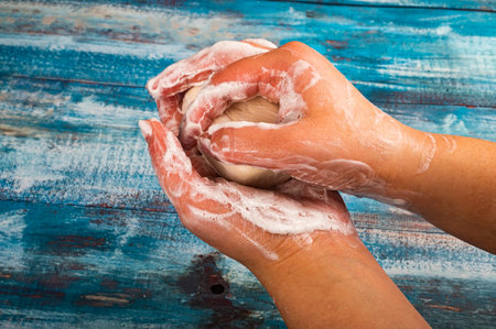Someone is soaping their hands with a piece of toilet soap on a wooden background. Close up. Washing...