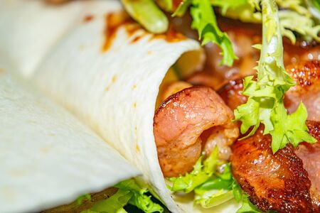 Leafy salad, sliced vegetables, sauce and fried bacon slices wrapped in pita bread. Delicious homemade Shawarma. Close upの写真素材