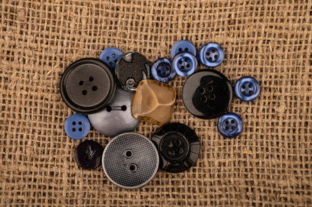 Several multi-colored buttons of different sizes on a background of coarse-textured burlap. Close up