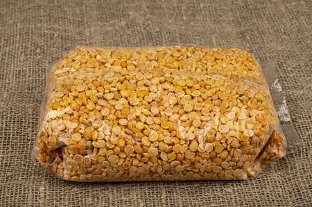Yellow split peas in a cellophane bag on a background of coarse-textured burlap. Traditional grains for making soups and porridges. Close upの写真素材