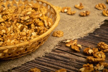 Peeled walnuts in a wicker basket and peeled walnuts scattered on a wooden table covered with rough-textured burlap. Healthy diet. Fitness diet. Close upの写真素材