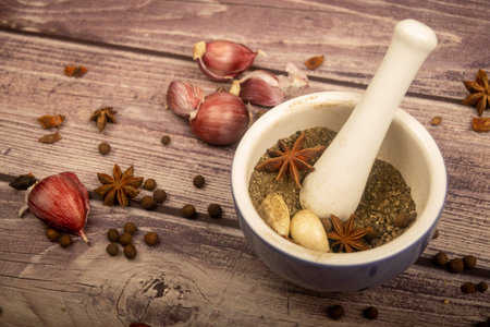 Allspice in a ceramic mortar and scattered garlic cloves, star anise and allspice on a wooden table....