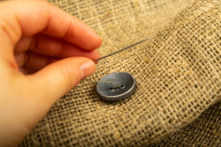A girl's hand sewing a black button to a piece of burlap. Close up