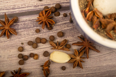 Allspice in a ceramic mortar and scattered garlic cloves, star anise and allspice on a wooden table. Close upの写真素材