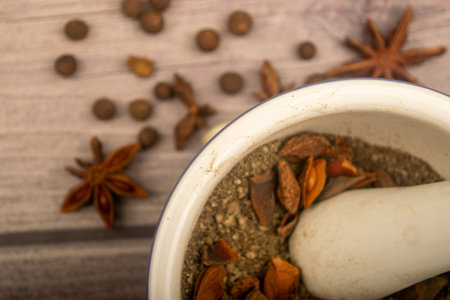 Allspice in a ceramic mortar and scattered garlic cloves, star anise and allspice on a wooden table....